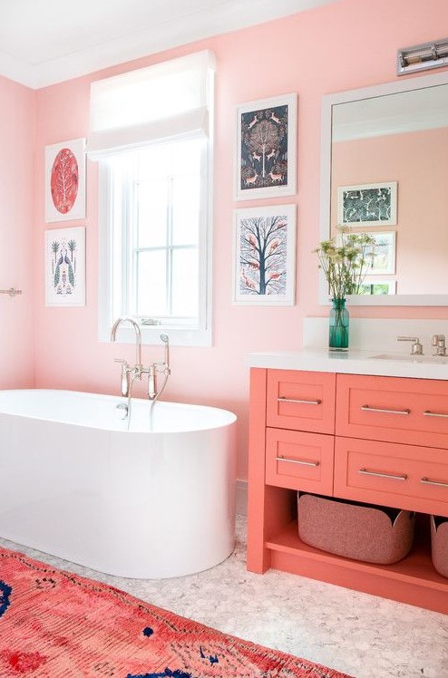 A pink bathroom with pink walls, a coral vanity, a bright printed rug and a fun gallery wall is a very whimsy space.