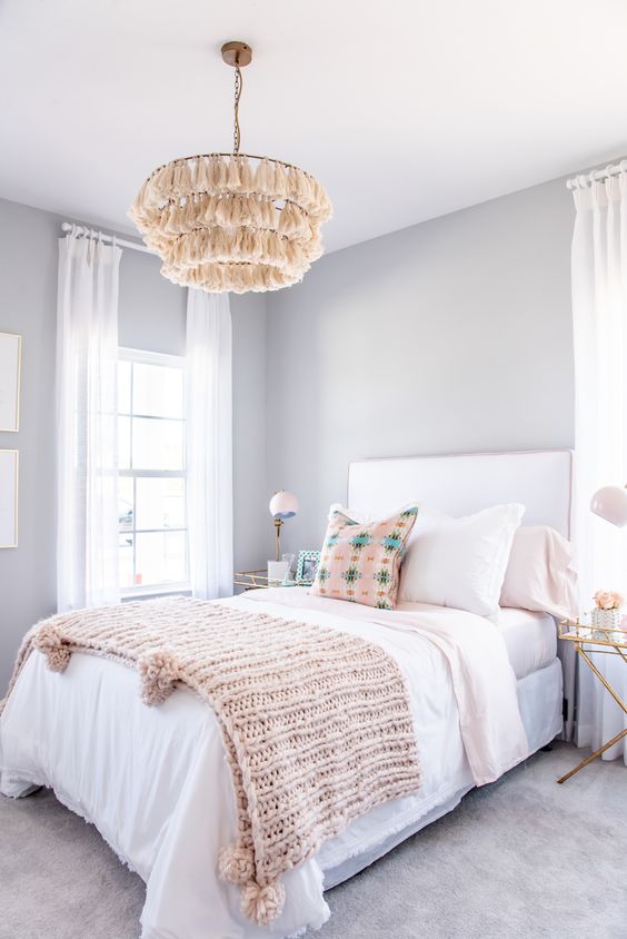 A pretty and relaxed teen girl bedroom with light grey walls, a white bed with pastel bedding, nightstands and tassel chandeliers.