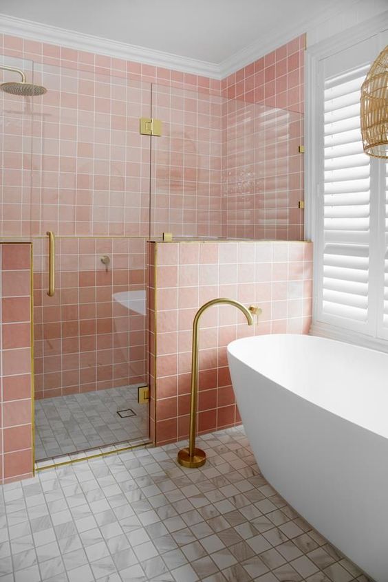 A pretty bathroom with pink and white square tiles, a shower space, an oval tub and gold fixtures is lovely.