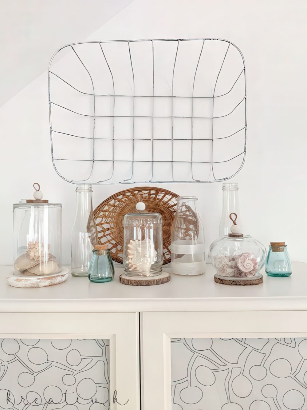 A pretty beach display with seashells and corals in jars and cloches plus blue bottles and a wicker basket.
