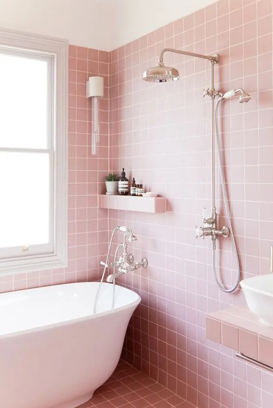 A white tub and sink stand out in this pretty pink bathroom clad with square tiles. A built-in shelf and a vanity with lights add practicality and style. Choose classic tiles and built-in features for a neat and charming bathroom.