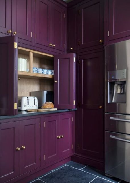 A purple kitchen with a cabinet with folding doors and some appliances hidden there plus some mugs to make breakfast.