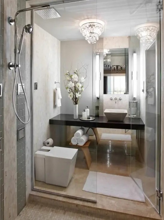 A refined small bathroom with stone tiles, a crystal chandelier, a shower space and a built-in dark vanity.