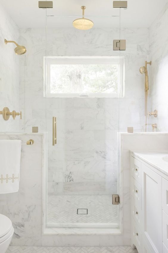 A refined white marble bathroom with half walls int he shower space and touches of gold for a more chic look.