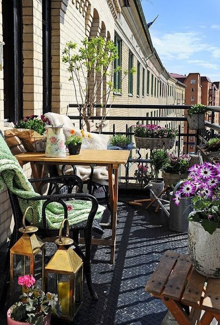 A refreshing summer balcony with potted greenery and blooms, rattan and wooden furniture, candle lanterns and textiles.