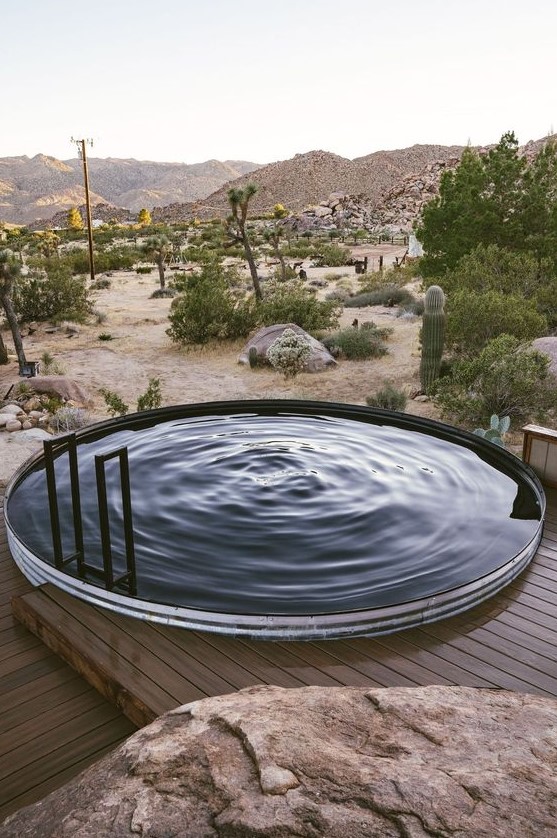 A round pool made of a stock tank, with a ladder and a wooden deck around it plus a view of the desert is a lovely space to spend time.