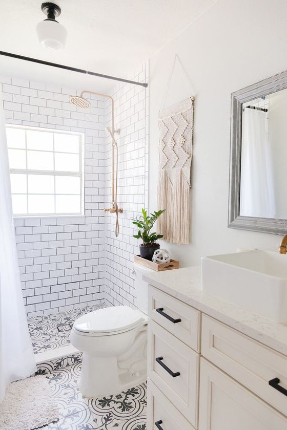 A small and neutral boho bathoom with white subway tiles and black and white ones, a farmhouse vanity, a macrame hanging and touches of black.