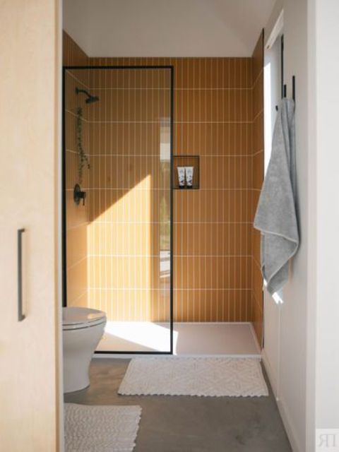 A small and bright bathroom with a shower space clad with yellow skinny tiles, a concrete floor and white appliances welcomes in.