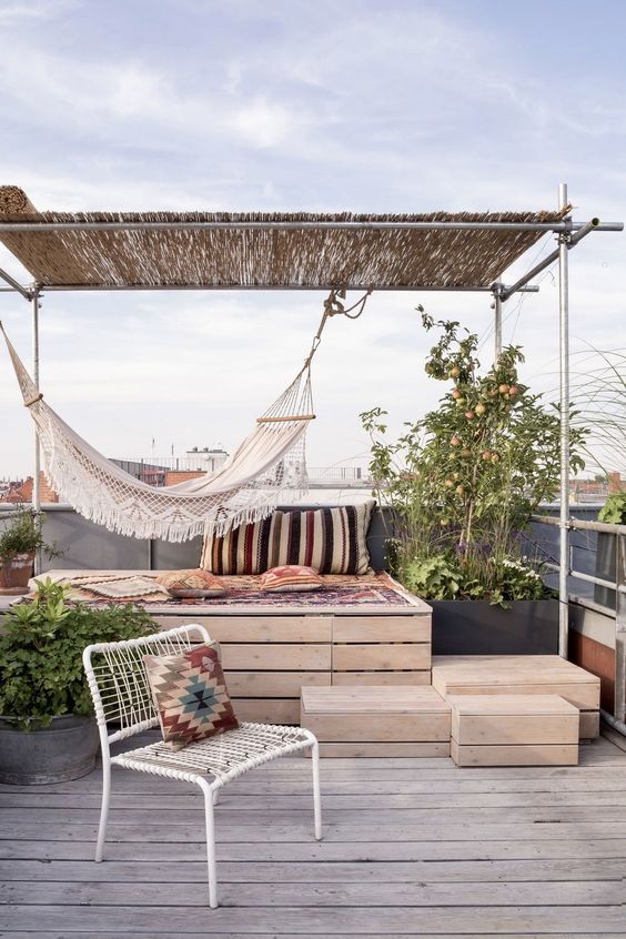A small and simple terrace with a storage daybed, a metal chair, boho textiles, a hammock and some greenery in pots.