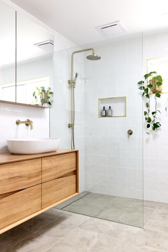 A small, welcoming modern bathroom features white and grey tiles. A catchy wooden vanity, a mirror cabinet, and brass touches complete the look.