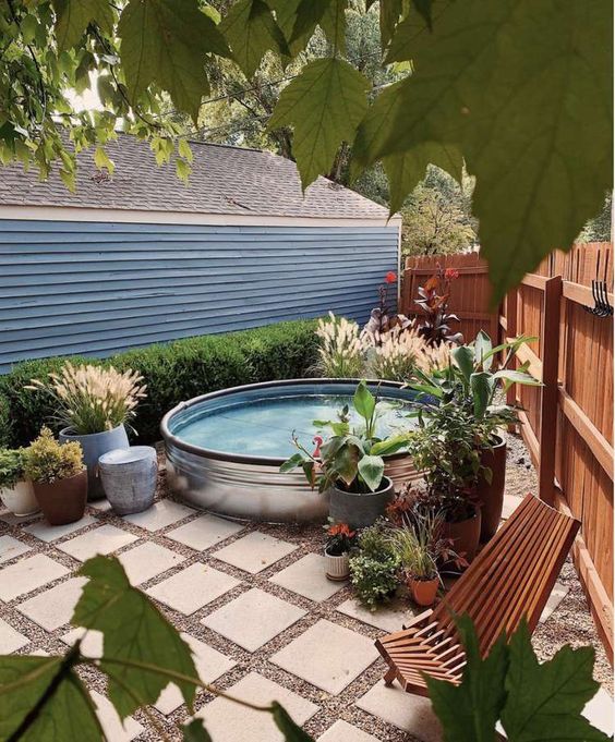 A small backyard clad with tiles, a stock tank pool, wooden loungers, potted plants and blooms is a lovely nook to have a rest in.
