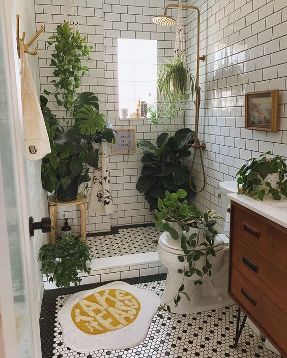 A small boho bathroom clad with white subway tiles, with black and white penny ones, with lots of plants for a forest feel.