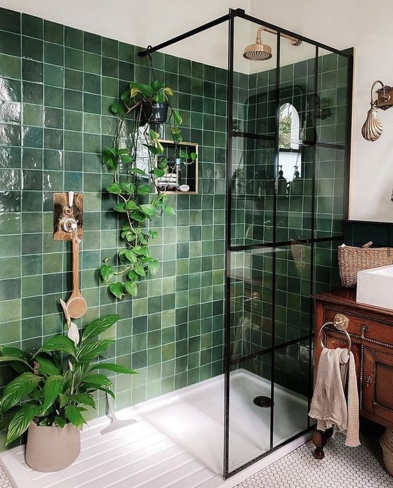 A small bright bathroom with green square tiles, a vintage stained vanity, white appliances and penny tiles on the floor plus potted plants.
