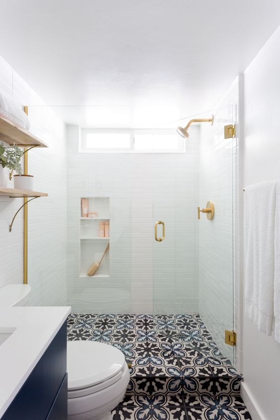 A small contemporary bathroom with white tiles in the shower, patterned tile floor, a navy vanity and touches of gold.