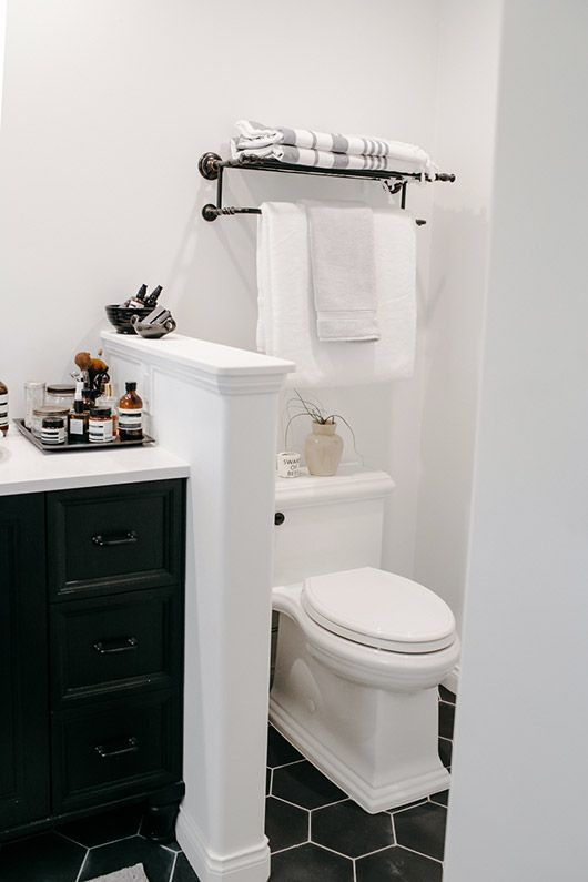 A small farmhouse bathroom clad with black hex tiles on the floor, with a half wall to separate the toilet and a black vanity.