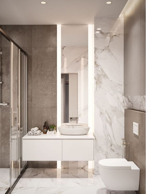 A small minimalist bathroom with marble tiles, a shower space, a floating vanity and a tall mirror with lights.