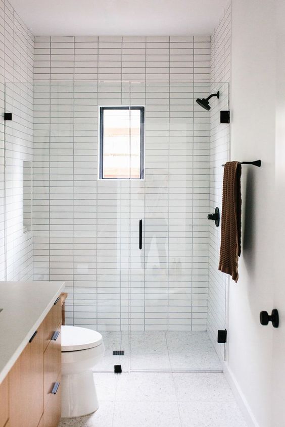 A small minimalist bathroom with neutral tiles, with skinny ones and printed ones on the floor, a small window and black fixtures for a modern feel.