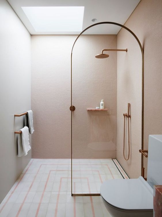 A small minimalist bathroom with pink walls, a printed tile floor, a glass divider and touches of rose gold.