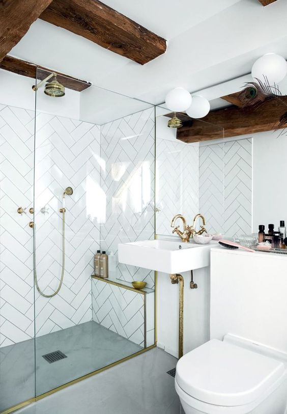 A small yet cool bathroom with white herrignbone tiles, dark wooden beams, gold fixtures for a luxurious touch.
