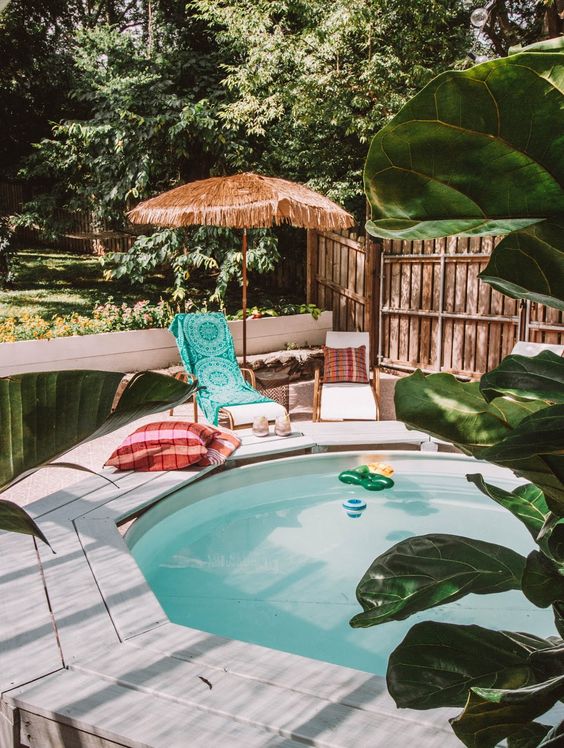 A stock tank pool, a wooden bench, loungers and pillows, floats and greenery around, an umbrella is cool.