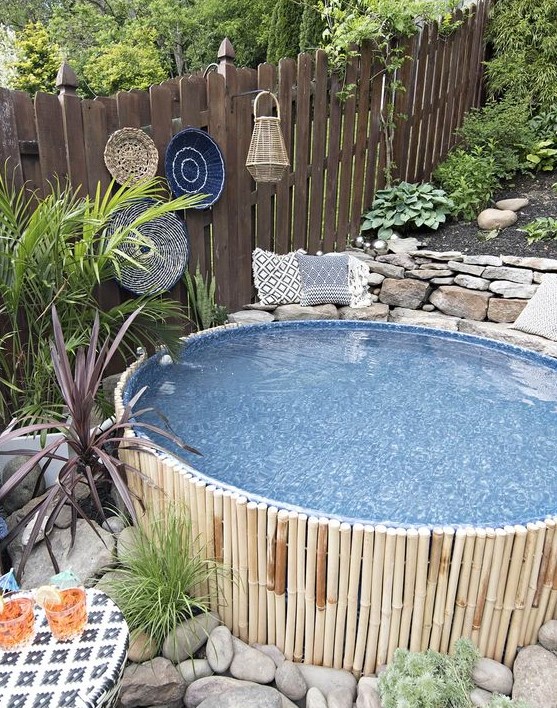 A stock tank pool covered with bamboo, with decorative baskets and a candle lanterns, large rocks and growing plants.