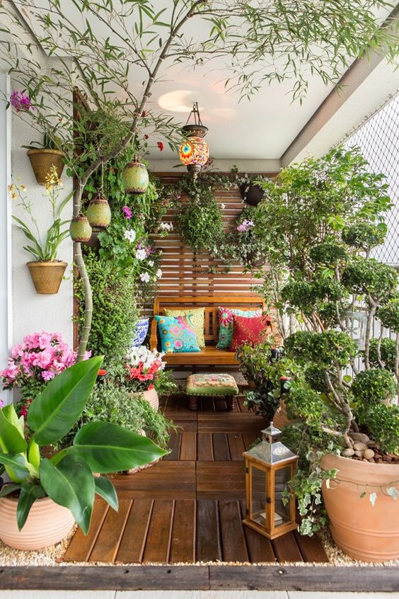 A summer balcony turned into a garden, with potted blooms and greenery, candle lanterns and some wooden furniture.