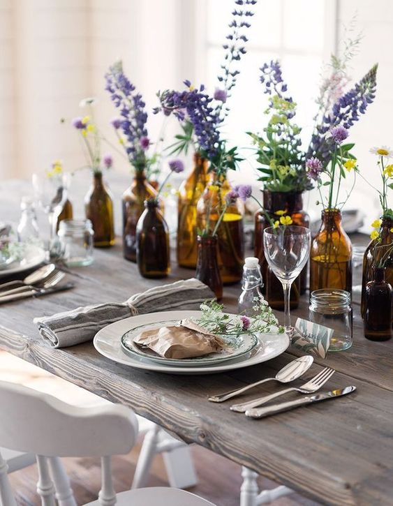A summer table lined up with apothecary bottles and jars with bright blooms in them for a beautiful look.