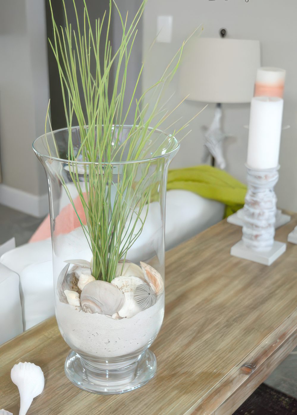 A tall glass with beach sand, seashells and some grass for decorating your console table.