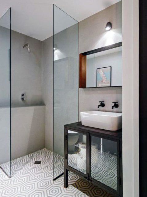 A tiny bathroom with concrete walls and printed tiles on the floor, a small shower space, a black vanity and a sink.