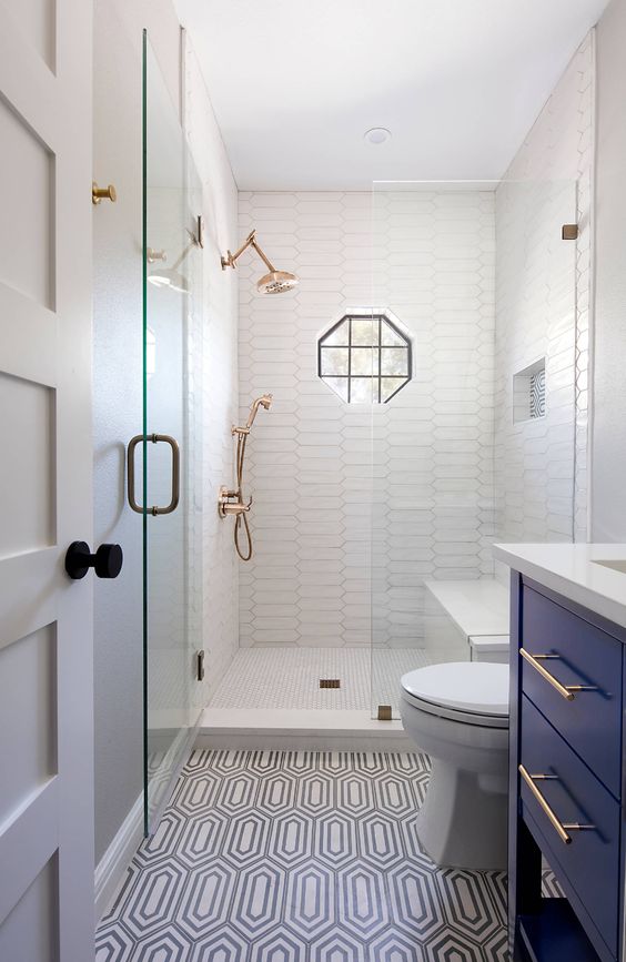 A tiny bathroom features white and printed tiles, a navy vanity, and white appliances. Brass fixtures and black touches enhance the design.