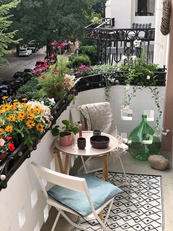 A tiny summer balcony with lots of potted blooms, wooden and metal furniture and pretty accessories.