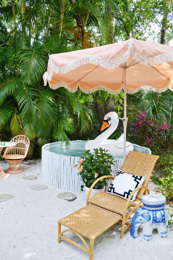 A tropical outdoor space with a stock tank pool with bamboo, rattan chairs and loungers, some bright decor and blooms.