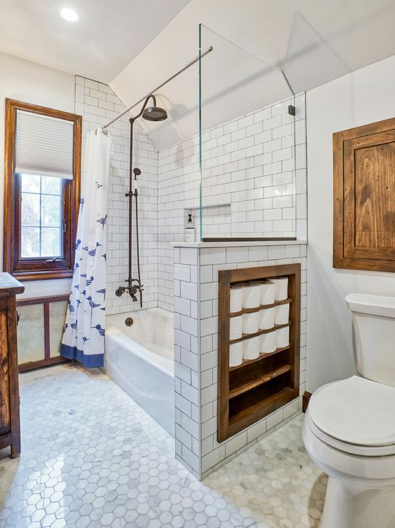 A vintage-inspired bathroom with white and marble tiles, with a half wall that has soem integrated storage space, touches of stained wood for more coziness.