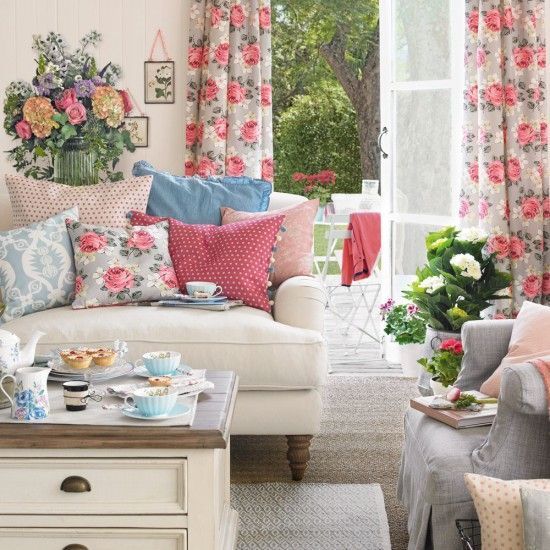 A vintage-inspired living room with florla curtains, printed pillows, potted blooms and greenery and bright blankets for summer.