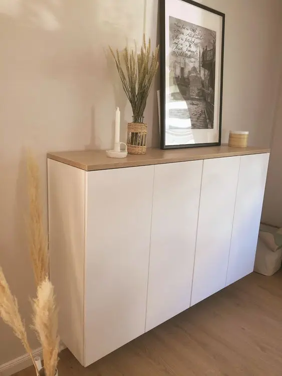 A white floating credenza of IKEA Metod with a butcherblock countertop, an artwork, a candle and decor.