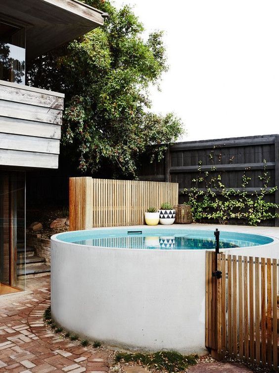 A white stock tank pool with a deck, a wooden fence and some potted plants and greenery around it.