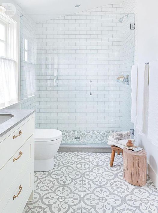 An airy neutral bathroom features white subway tiles and printed floor tiles. A white vanity, a stool, and a tree stump add natural charm.