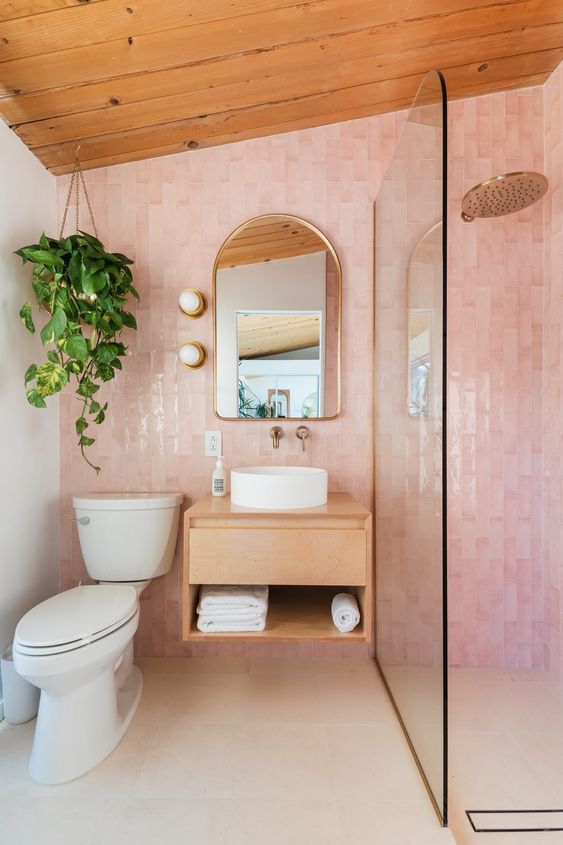 An attic bathroom with a blush tile accent wall, a shower space, a floating vanity, an arched mirror and a potted plant.