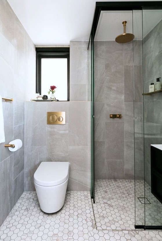 An elegant contemporary bathroom with stone and marble tiles, a window, a shower space and gilded touches.