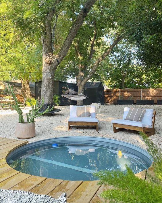 An outdoor space with a gravel yard, seats, an in-ground stock tank pool, potted greenery is amazing.