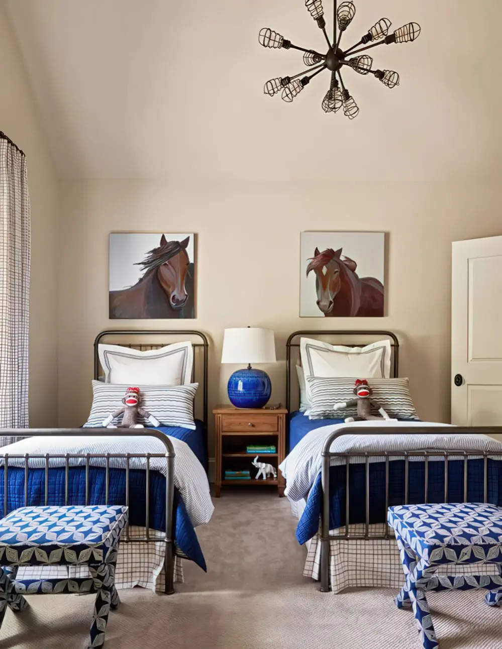 A charming country-style bedroom featuring twin iron beds, horse artwork, and blue-and-white patterned accents. The classic color scheme and rustic furniture create a cozy yet sophisticated retreat.
