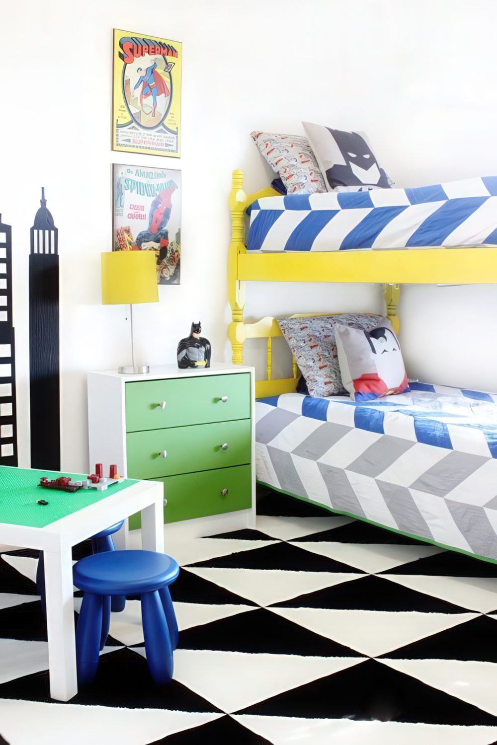A vibrant, comic book-inspired boys' room with a yellow bunk bed, bold striped bedding, and graphic artwork featuring Superman and Batman. The green and blue accents add a playful touch, while a LEGO-building station completes the fun atmosphere.