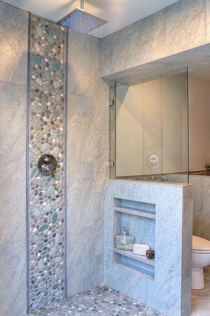 A neutral bathroom clad with tiles and faux pebbles, with a pony wall that had some shelves integrated is a lovely space.