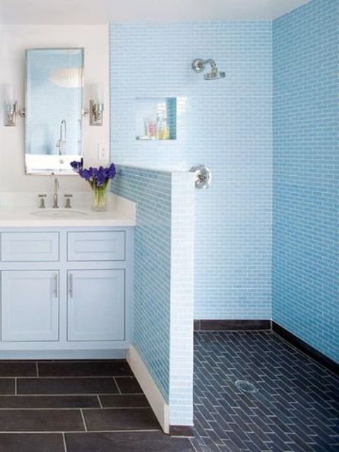 A blue bathroom with a navy tile floor in the shower, light blue tiles in the shower space and a light blue vanity is chic.