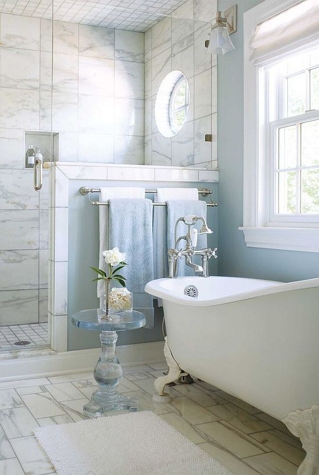 A beautiful bathroom with blue walls and a shower space clad with marble tiles, with a vintage bathtub and a pony wall in the shower space.