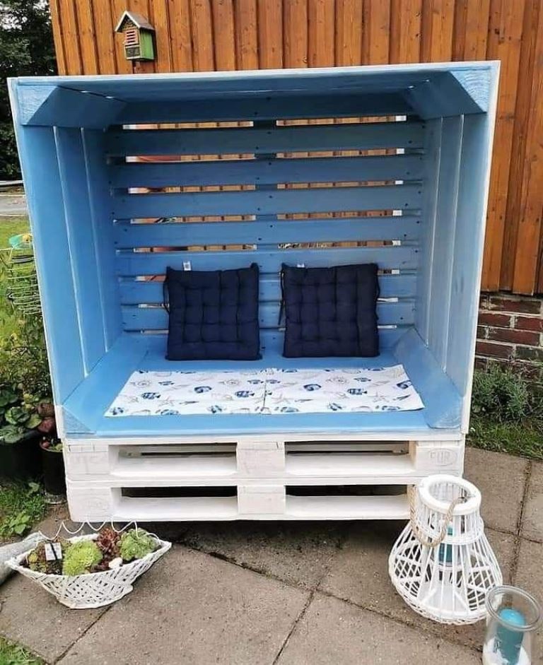 The arbor is made of pallets and painted light blue and white, with upholstery and lanterns and decor around.