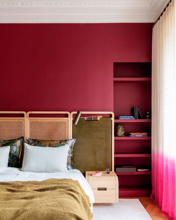 The super bright bedroom is done with berry-hued walls and built-in shelves, a bed with a cane screen headboard and a leather panel with a lamp.