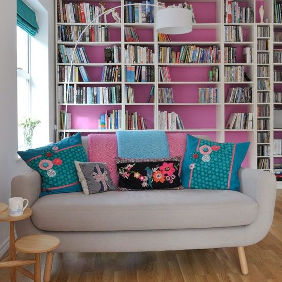 A bold hot pink wall, turquoise shades and matching colorful pillows make this living room feel like summer.