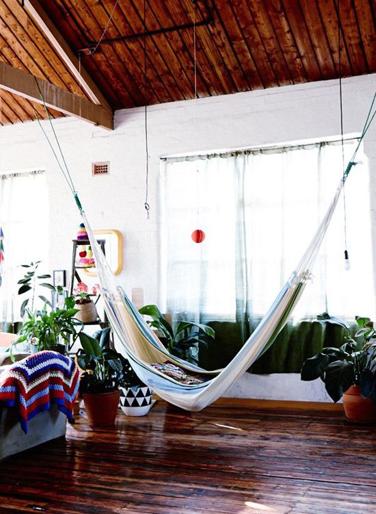 A bright and cheerful summer living room look is achieved with potted greenery, bright textiles and a hammock hung in the center of the room.