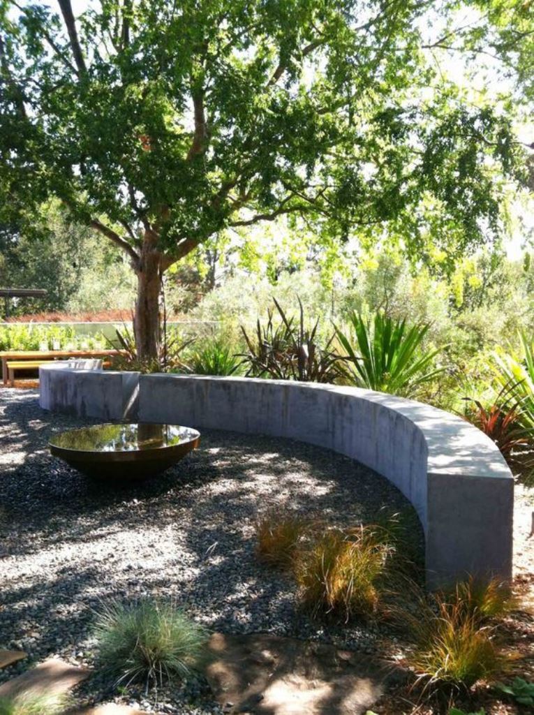 The contemporary space shows off plants, a tree and a curved concrete slab bench with a water bowl.
